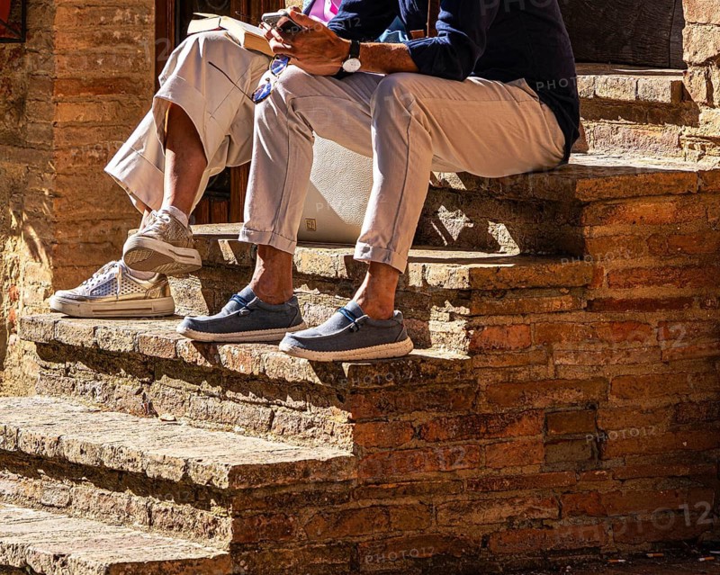Two tourists sit on the steps of a stone staircase, Pienza in Tuscany, Italy