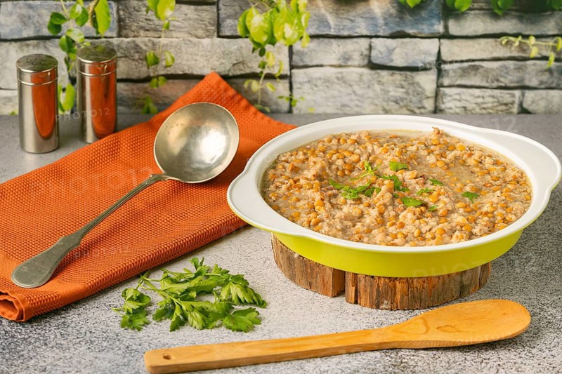 Lentils with bacon in a bowl with a ladle next to it, rustic stone wall in the background