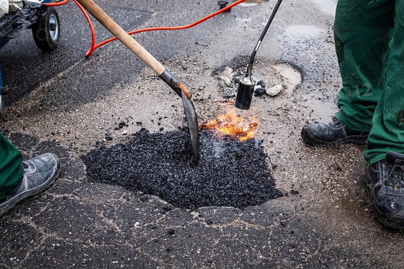 Road workers repair a pothole on a street by pouring hot asphalt from a bag and smoothing it with a torch and shovel in Poland