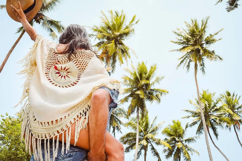 Happy young couple piggyback walking having fun on sandy pathway under tall coconut palm trees generic tropical island beach resort sunny summer day