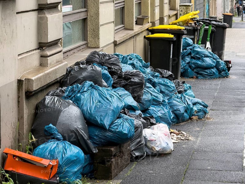 Mountains of trash made of blue and black bags pile up along a house façade on the sidewalk, Wuppertal, Germany