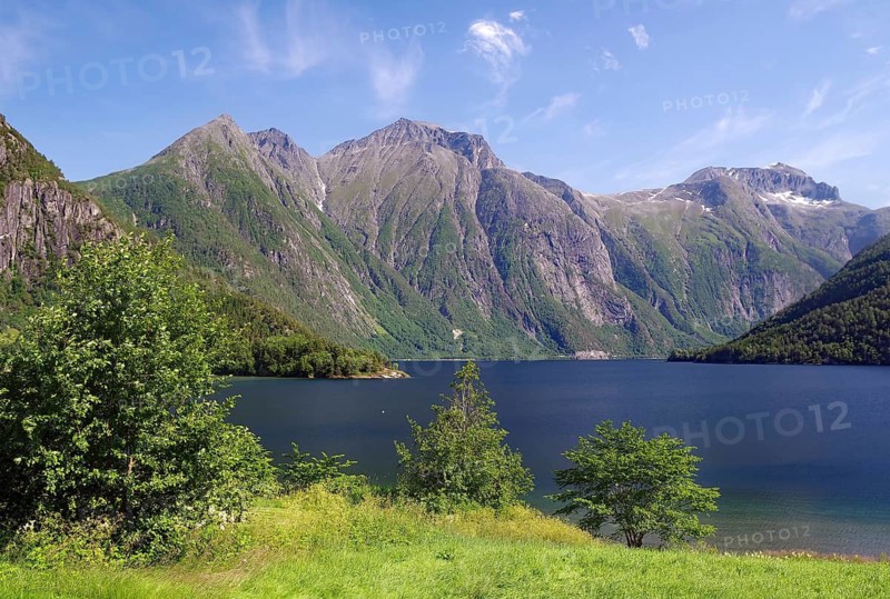 View of a mountain lake surrounded by high mountains and green forest under clear skies, Eikesdalvatnet, Aursjövegen, More og Romsdal, Norway