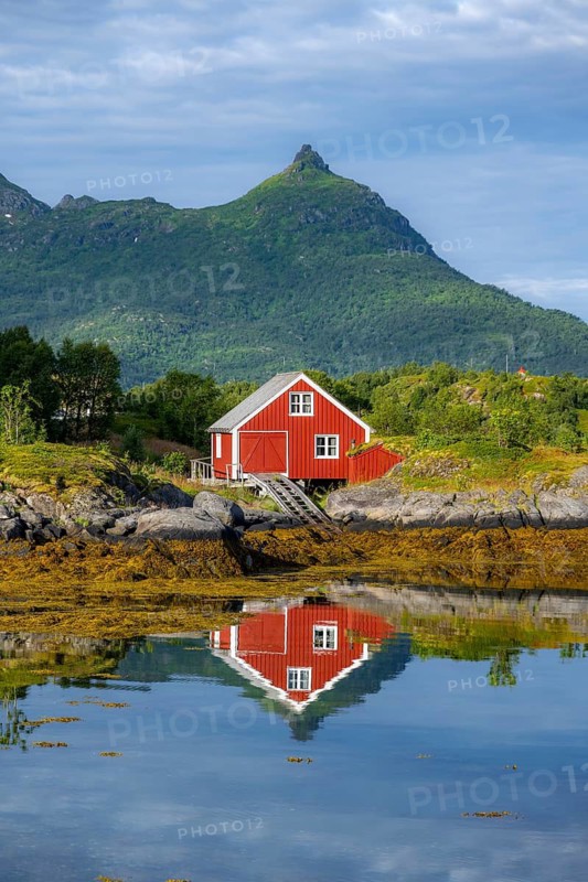 Red fishing hut on the shore, Rorbuer hut, picturesque fjord landscape at Raftsund fjord, mountains reflected in water, Vesterålen, Norway