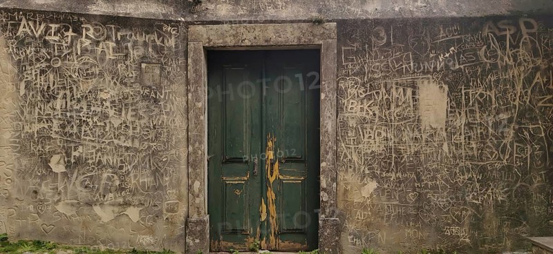 Weathered green wooden door in a gray wall with lots of graffiti and doodles, Sintra-Cascais Natural Park, Lisbon, Portugal