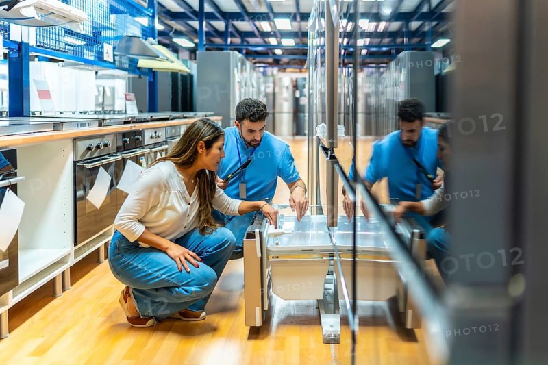 Woman customer and a male salesperson are discussing kitchen appliance features. Shopping for home renovations in a modern retail showroom. Showcasing customer service and sales assistant interaction