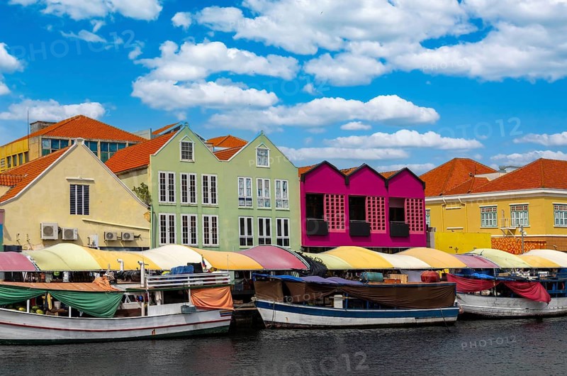 Traditional boats at the floating market in front of vibrant colonial architecture in the Punda district of Willemstad Curacao under a blue cloudy sky