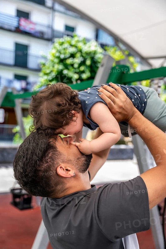 Happy father lifting cute toddler son in his arms, sharing a moment of joy and affection outdoors in a playground, representing family bonding and love