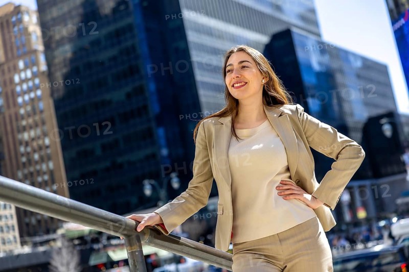 Businesswoman in a smart blazer stands outdoors in manhattan, smiling confidently as she looks toward the bright city skyline, symbolizing ambition, leadership and career growth