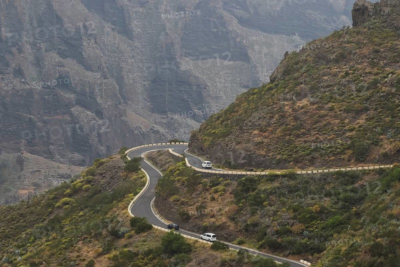 Steep serpentine road with cars snaking along a rock wall surrounded by vegetation, Masca, Barranco de Masca, Gorge, Teno, Teno Mountains, Northwest Tenerife, Tenerife, Canary Islands, Spain