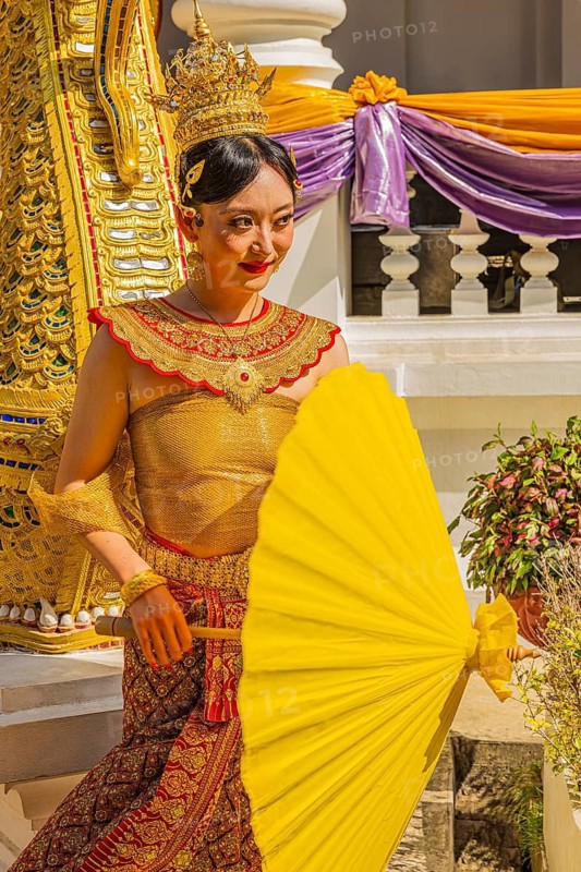Young Thai woman in traditional clothing and yellow parasol poses in front of photographers at the Wat Phra Singh Buddhist temple complex, Chiang Mai Old City Center, Chiang Mai Province, Thailand