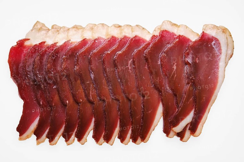 Cured duck meat in a row on a plain white background. Each slice shows rich color and texture. This scene captures the preparation of food for serving or tasting
