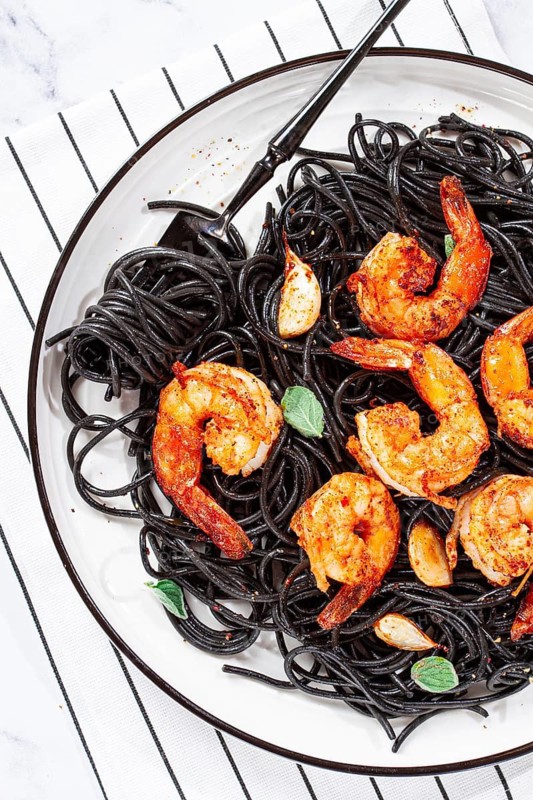 Black spaghetti with shrimp, on a white plate with a fork, on a striped napkin, marble background, homemade, no people