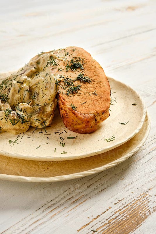 Grilled meat served with creamy mushroom sauce and herbs on simple plate at kitchen table