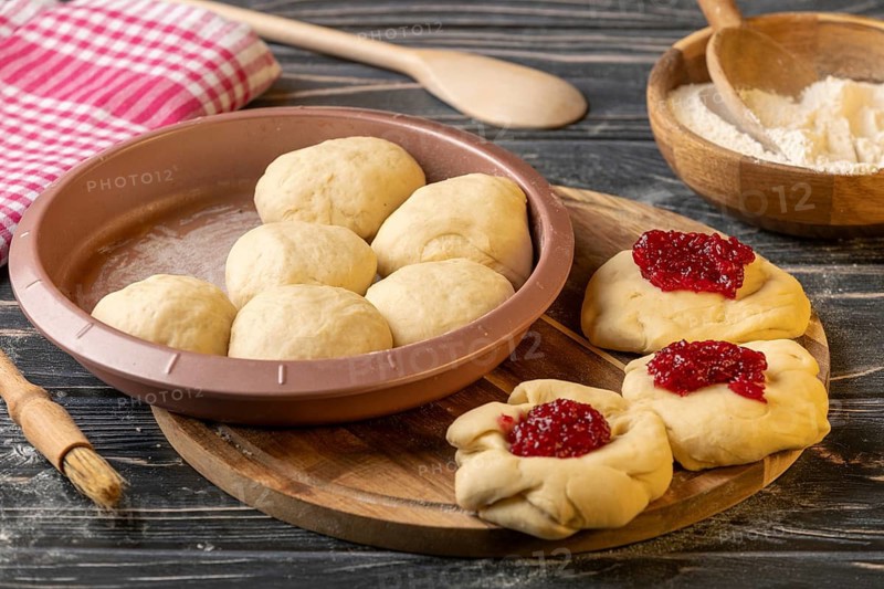 Dough pieces filled with marmalade in and next to the baking pan