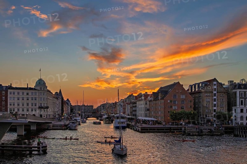 Farbenfroher Sonnenuntergang über einer Stadt mit Kanal und Booten unter einem dramatischen Himmel, Kopenhagen, Dänemark, Nyhavn