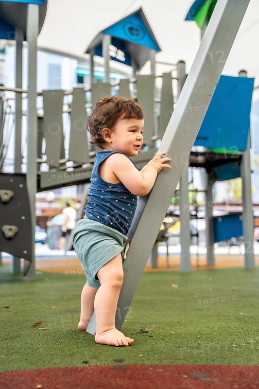 Adorable toddler boy, full of innocence and curiosity, exploring and learning to stand by holding onto outdoor playground equipment, enjoying active childhood fun in the park