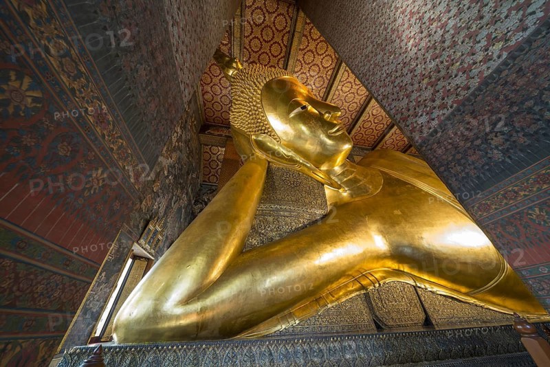The monumental reclining Buddha shows the moment of entry into Nirvana. Golden surfaces, delicate patterns and warm temple colors accentuate the spiritual peace of this iconic depiction, Wat Pho, Bangkok, Thailand