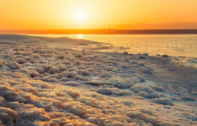 Close up Dead Sea salt crystals on shoreline beach in Jordan at sunset with turquoise water desert coast lowest point on Earth landscape. Jordan - Israel border line zone