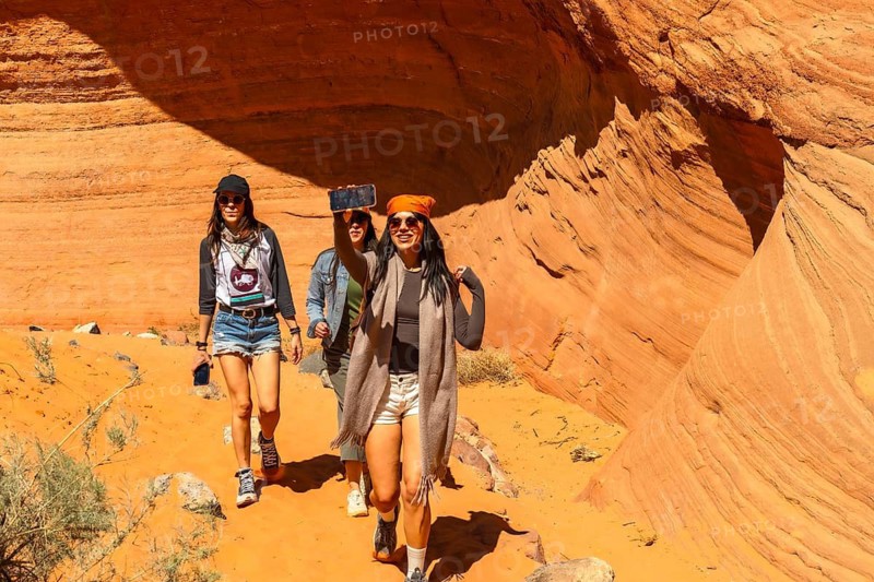 Women hikers enjoying an outdoor adventure, taking a selfie inside the famous biidi the arch cave near page, arizona, surrounded by unique sandstone formations and vibrant desert hues