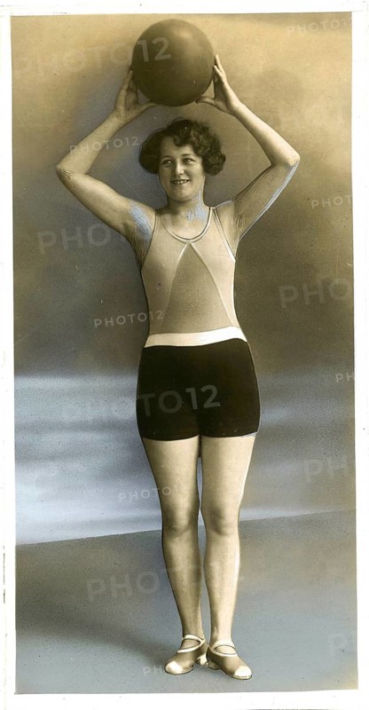 Swimwear, England, woman in swimsuit holding a ball over her head and posing in studio, hand-colored, around 1926