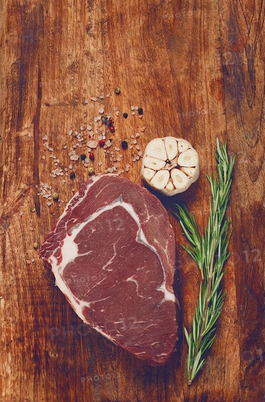 Raw steak, beef steak, rib eye steak, on a cutting board, freshly frozen, with spices and herbs, on the table, top view