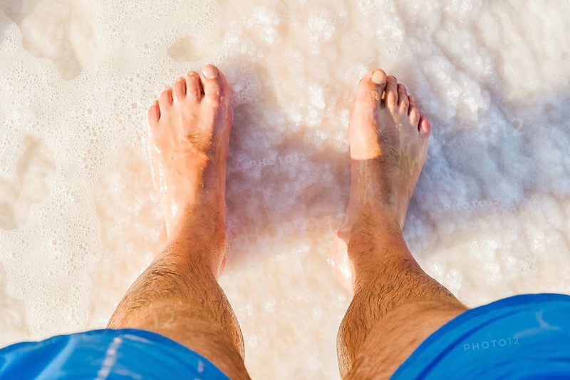 Close-up POV male tourist walking on the unique salt formations and turquoise mineral-rich waters of the Dead Sea beach. A concept for wellness, healthy living, and natural spa travel
