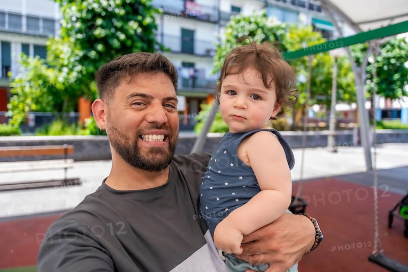 Father holding his young son at an urban park playground, smiling and embracing while enjoying a sunny day out, capturing playful bonding and family memories