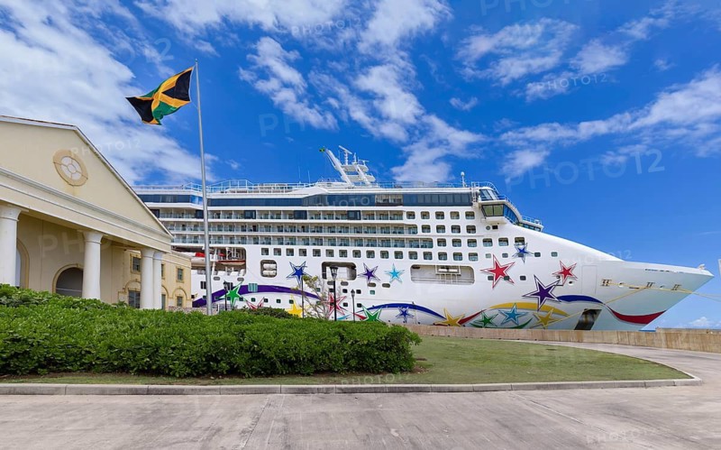 A large Caribbean cruise ship decorated with colorful star pattern on its hull docked at Falmouth cruise terminal, Jamaica, with a Jamaican flag flying in the foreground
