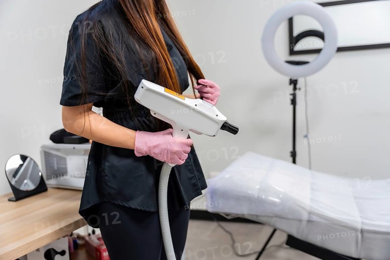 Medical specialist in pink gloves holds a modern laser device over a clinic table, preparing for a cosmetic laser treatment such as tattoo removal or skin rejuvenation procedure