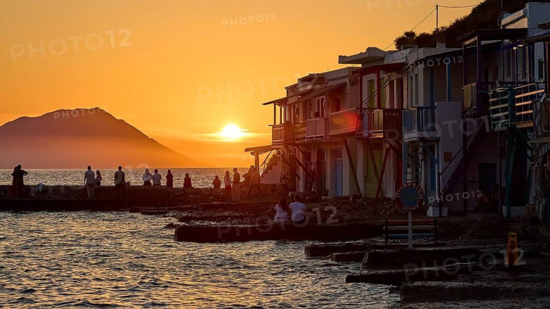 Evening atmosphere by the sea with silhouettes and colorful buildings at sunset with warm light, boathouses, boat garages, Syrmata, fishing village, coastal town, climate, Milos, Cyclades, Greek islands, Greece
