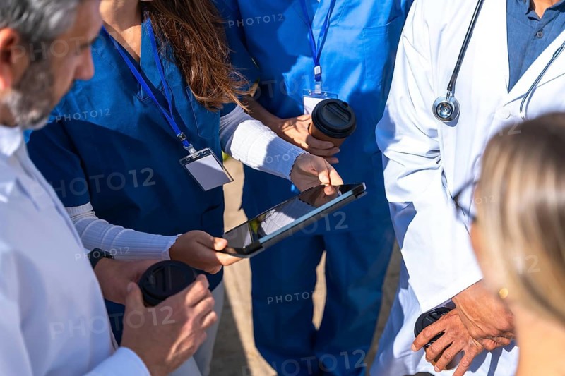Medical team of doctors and nurses collaborating, reviewing data on a digital tablet, and discussing patient cases, symbolizing teamwork, innovation, and modern healthcare technology outdoors