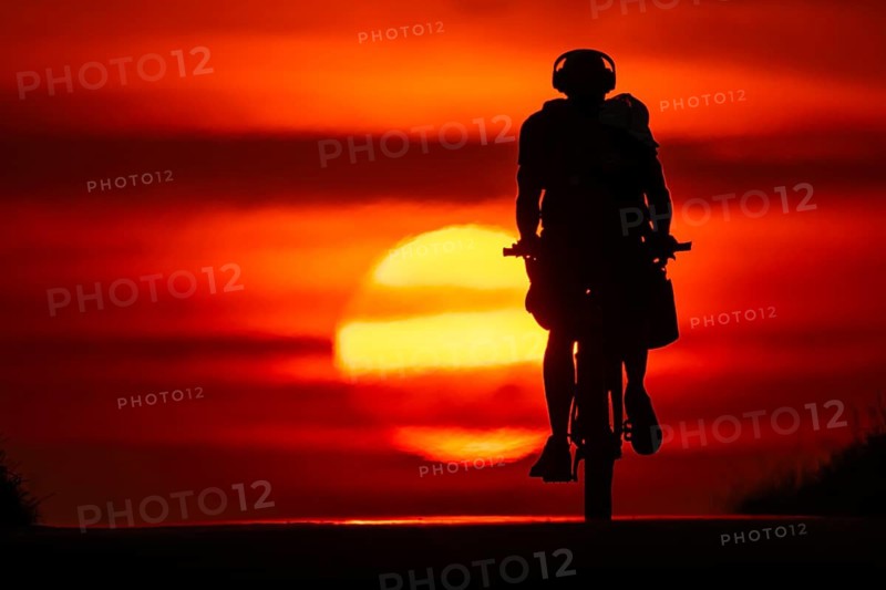A cyclist rides towards the rising sun on a dirt road near Frankfurt am Main, Frankfurt am Main, Hesse, Germany