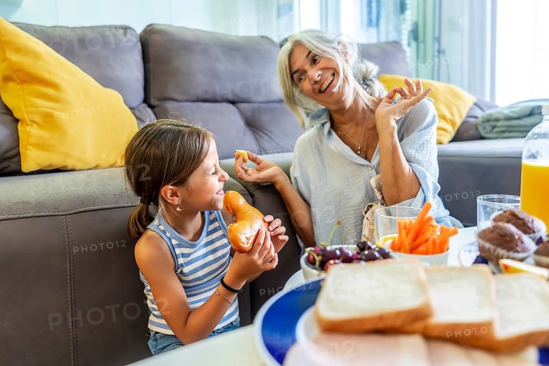 Grandmother and granddaughter smiling and laughing while eating a healthy snack and breakfast food together, creating a beautiful bonding moment in a home setting