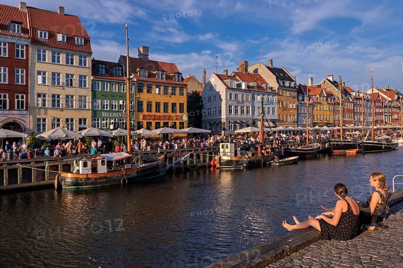 Lebendiges Treiben entlang eines Kanals mit bunten Häusern und Booten bei Sonnenschein, Kopenhagen, Dänemark, Nyhavn
