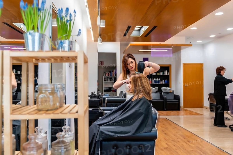 Female stylist blow drying and brushing a client's hair in a modern salon, providing professional styling and personalized beauty treatment with expert care and attention to detail