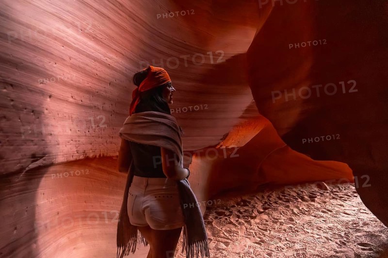 Woman standing inside a slot canyon, admiring the natural geological formations of sandstone walls carved by water and wind, creating a unique desert landscape