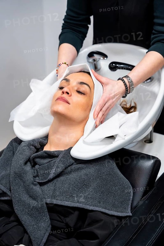 Woman with closed eyes relaxed at a salon basin as hairdresser shampoos and massages her hair, enjoying a soothing beauty and wellness treatment during a pampering service
