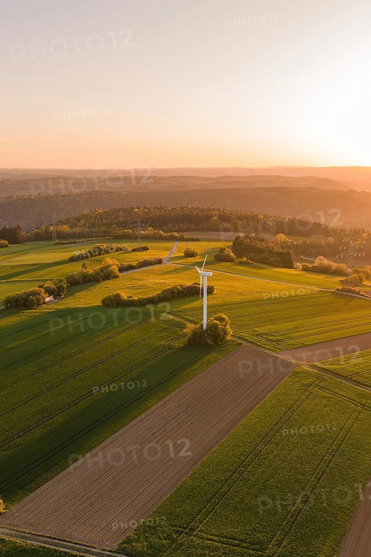 Wide green fields with a wind turbine, under brilliant sunset, gently rolling hills in the background, Jettingen, Germany