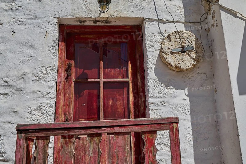 Weathered red wooden door in a stone wall with rustic charm and texture, Plaka, main town on Milos, Milos island, volcanic island, Cyclades, Greek Islands, Greece