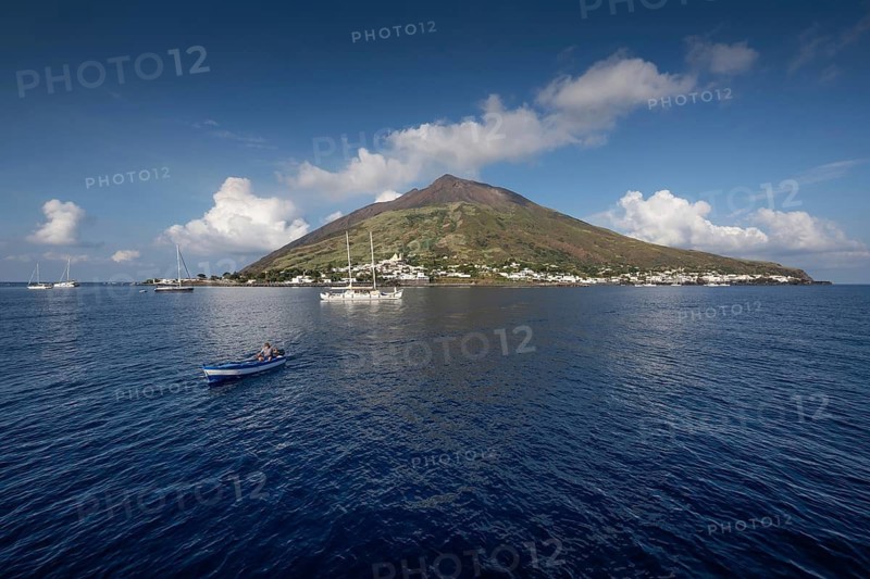 Island with volcano, boats on calm sea under blue sky, Stromboli, Aeolian or Lipari Islands, Southern Italy, Italy