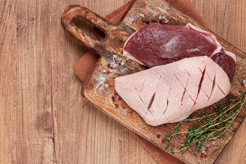 Fresh raw duck breasts, on a wooden chopping board, with herbs and spices, no people