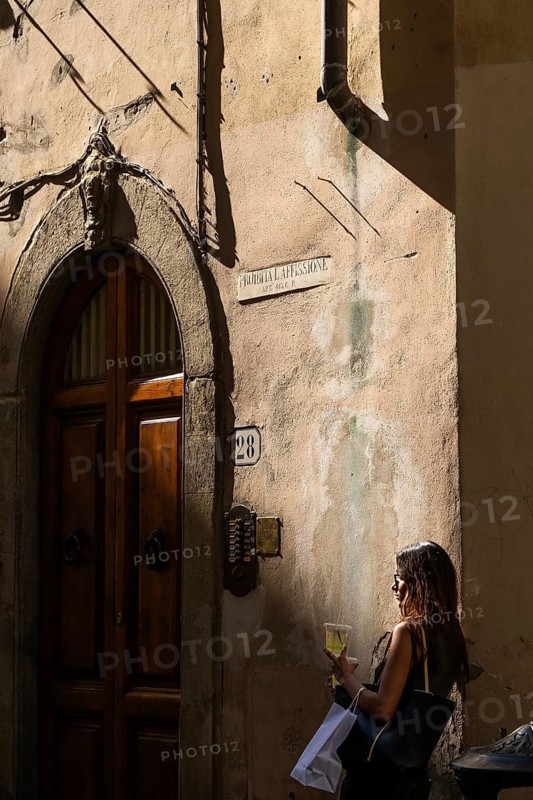 Woman leaning against a house wall with drink and shopping bag, Florence, Tuscany, Italy