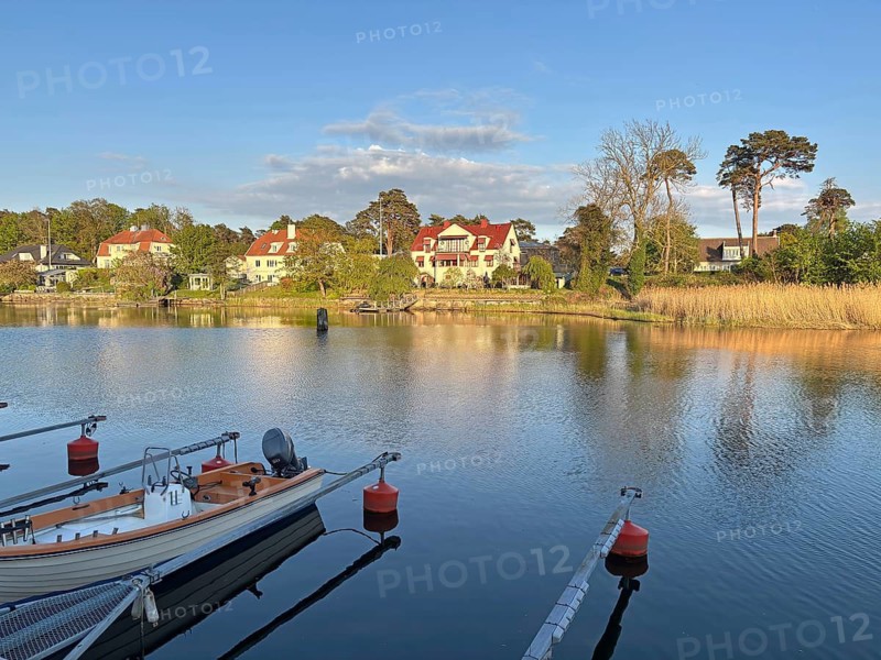 View of a quiet lake surface with a tranquil neighborhood in the background and trees under a blue sky, Ahus, Skane, Sweden