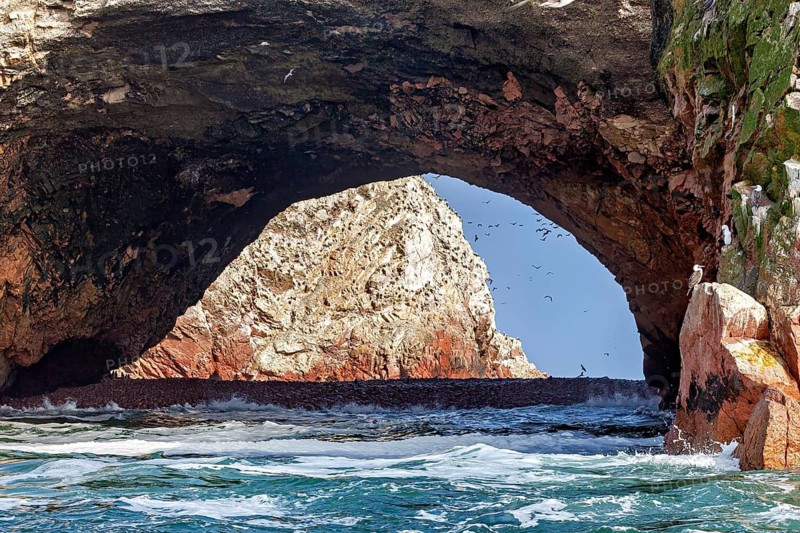 Natural rock arch over the sea with waves and blue sky, The rocky coast of Isla Ballestas near Paracas in Peru
