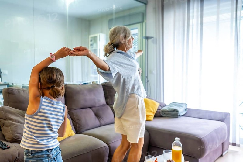 Grandmother and young granddaughter bonding, forming a strong family connection while enjoying a fun moment dancing and playing at home during their daily routine