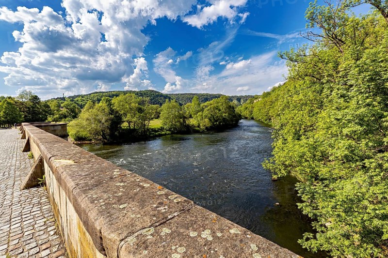 View of a river from a bridge, surrounded by green forest and under a blue sky with clouds, view of the Werra Valley near Creuzburg in Thuringia