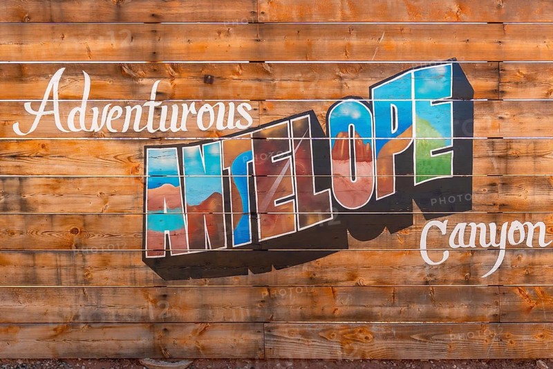 Wooden slatted fence displaying an adventurous antelope canyon text mural, featuring stylized letters with landscape imagery, highlighting tourism and travel to the popular arizona landmark