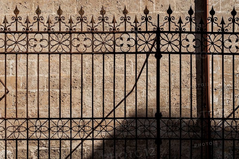 Cast iron fence with ornamental spikes, casting shadows on a stone wall, Palermo, Sicily, Italy