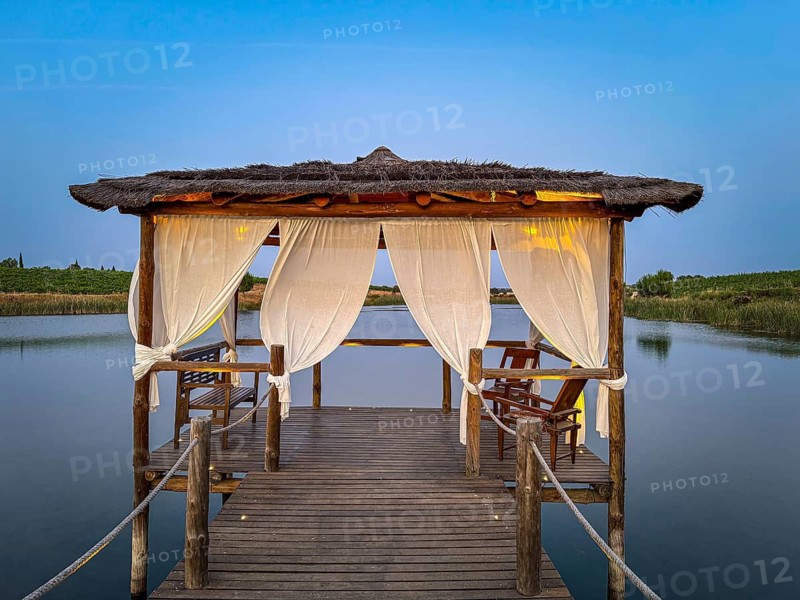 A rustic wooden pavilion with white curtains stands over a tranquil lake, Pedrógão, Beja, Portugal