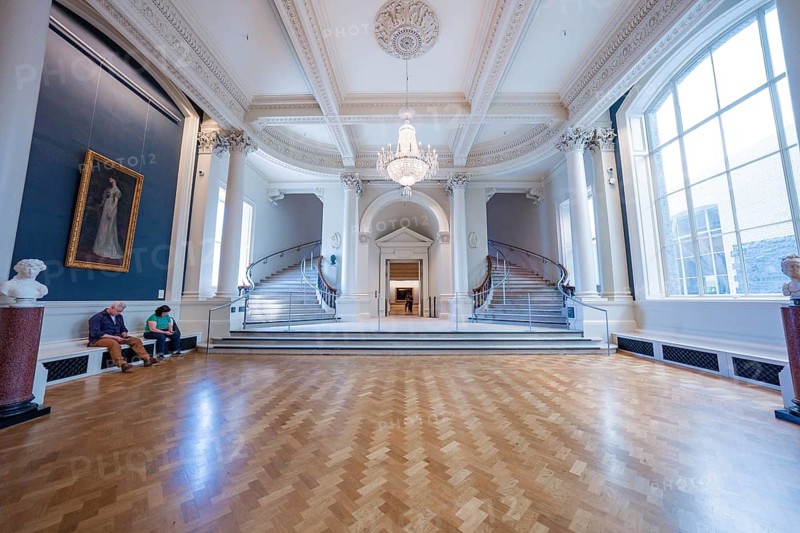 A room in a gallery with elegant stairs, chandeliers and parquet floors, occupied by seated people, National Gallery of Ireland, Dublin, Ireland